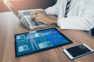 Medical provider works on laptop computer near a tablet showing remote patient monitoring information.